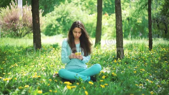 有电话的快乐女人坐在草地上视频的预览图