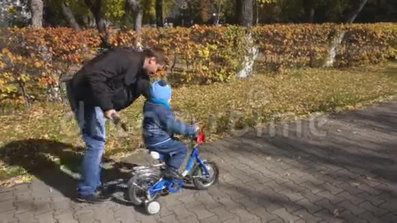 steadicam拍摄的父亲教儿子如何带着安全帽在公园路上骑自行车视频的预览图
