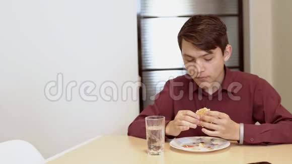 一个15岁的青少年咬一个三明治一个年轻人在桌子上吃三明治视频的预览图