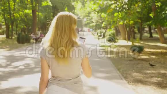 夏天在阳光下女人带着手机去公园4k慢镜头标准镜头视频的预览图