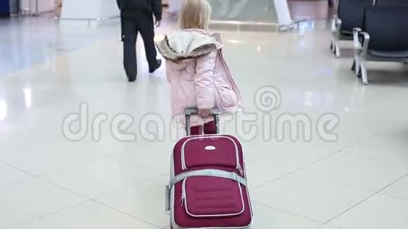 穿着冬装的金发小女孩带着手提箱穿过机场的候机大厅视频的预览图