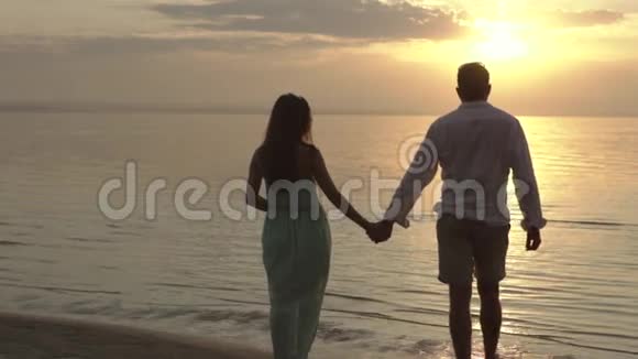 年轻快乐的一对夫妇在夕阳下漫步在海滩上爱的概念视频的预览图