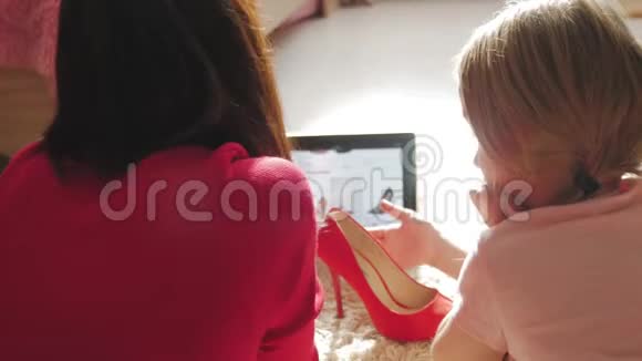 母亲和小女儿在数码平板电脑上网上购物时看鞋类网上购物的概念视频的预览图