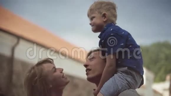 年轻的父母带着他们可爱的儿子在院子里接吻和玩耍视频的预览图