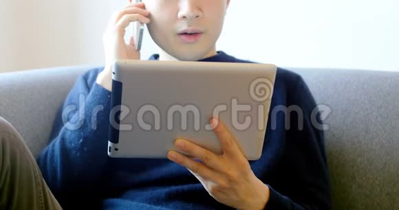 男子在客厅4k使用数码平板电脑时使用手机视频的预览图