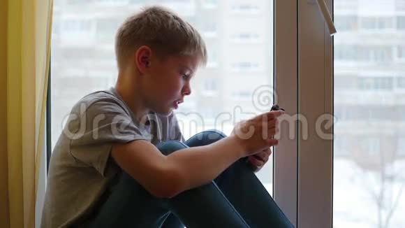 孩子坐在窗台上看着智能手机视频的预览图
