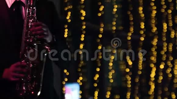成年男性在夜总会的舞台上玩萨克斯管背景上模糊的黄色bokeh灯视频的预览图