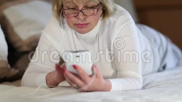 戴着白色智能手机眼镜的金发女人躺在床上视频的预览图
