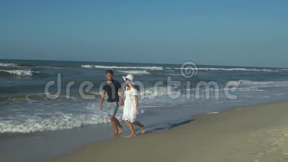 年轻漂亮的夫妇走在海边男孩和女孩他们很开心阳光灿烂慢动作海浪视频的预览图
