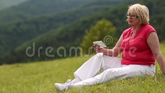 女人坐在绿草上听音乐视频的预览图