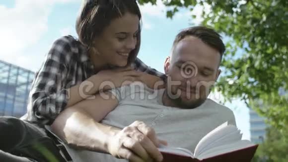 年轻的浪漫夫妇坐在公园里看书视频的预览图