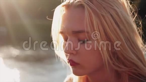 美丽的年轻白种人女孩在日落时在水前玩她的金发肖像慢动作视频的预览图