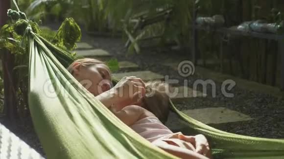 年轻的母女在夏日的花园里一起在吊床上放松视频的预览图