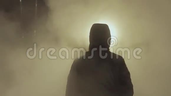头罩夹克中的男性剪影站在白色蒸汽云阻挡光点中视频的预览图