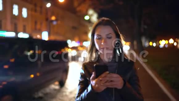 迷人的女人在夜城的街道上行走时使用智能手机视频的预览图
