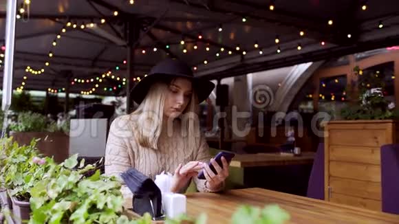 年轻女子打电话留言坐在装饰着圣诞灯的咖啡馆里视频的预览图
