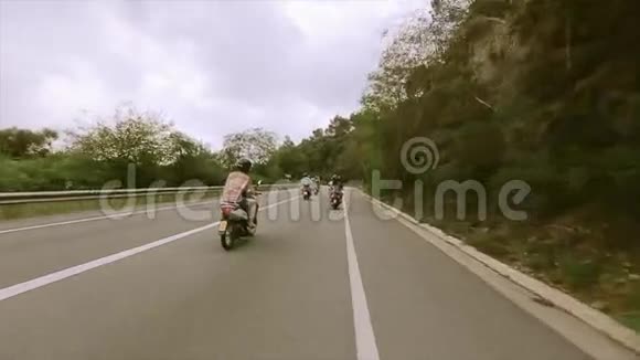 后面的人戴着头盔骑着摩托车在充满绿树的山丘之间的道路上旅行视频的预览图