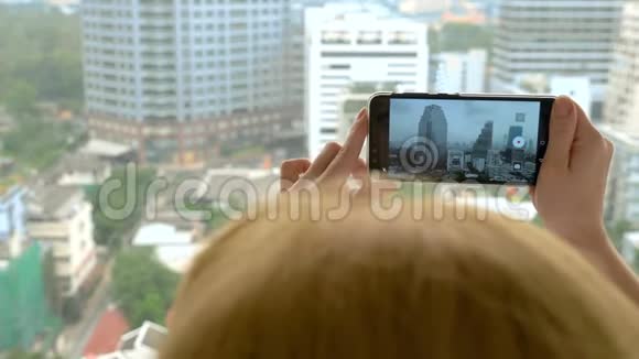 优雅的金发女人在电话里拍照女人从摩天大楼的窗户上拍摄风景视频的预览图