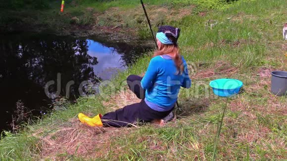 女孩在池塘里扔棍子在岸上钓鱼塔比猫走来走去视频的预览图