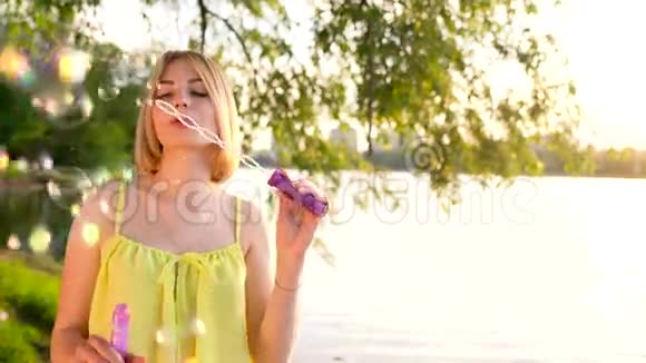 年轻漂亮的金发女郎在户外吹肥皂泡慢动作视频的预览图