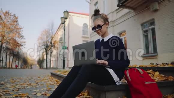 漂亮的时髦少女坐在秋城街的人行道上工作着笔记本电脑在校女生视频的预览图