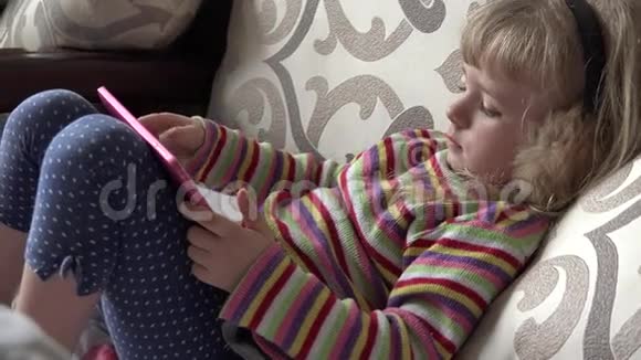 聪明的小女孩坐在沙发上用平板电脑4k超高清视频的预览图