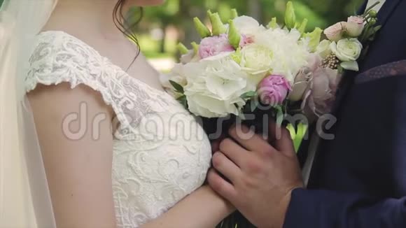 新娘和新郎捧着一束鲜花拥抱一束婚礼花束和双手特写视频的预览图
