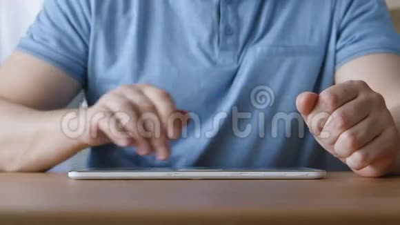 年轻人的手在家里的桌子上触摸平板电脑视频的预览图