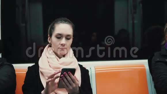 有魅力的女孩在地铁列车上使用智能手机年轻女子用触摸屏技术浏览互联网视频的预览图