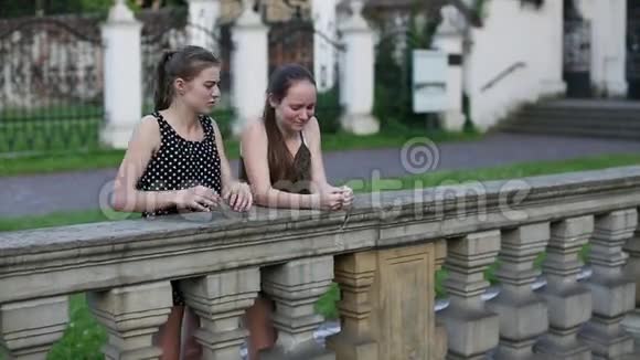 两个年轻的女孩站在石栅栏附近花时间交谈视频的预览图