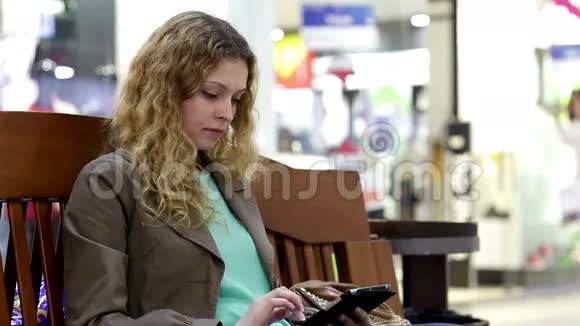 有平板电脑的年轻女子坐在商场的长椅上视频的预览图