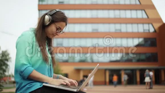 女孩在耳机上听音乐在笔记本电脑键盘上打字视频的预览图