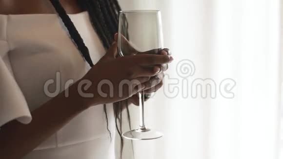 年轻的非裔美国女时装模特手里拿着空酒杯站在明亮的窗户附近手里拿着空酒杯视频的预览图