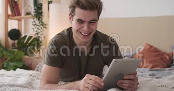 快乐男人在床上使用数码平板电脑视频的预览图