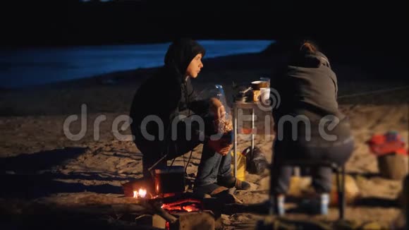 孩子们剪影孩子们坐在火边晚上在篝火旁吃爆米花旅行徒步旅行冒险露营视频的预览图