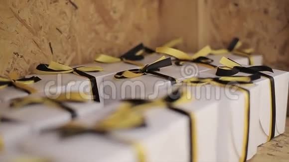 许多白色盒子系着黑色和黄色的蝴蝶结磁带停留在木制表面奖礼物节日视频的预览图