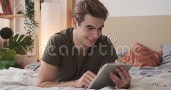 快乐男人在床上使用数码平板电脑视频的预览图