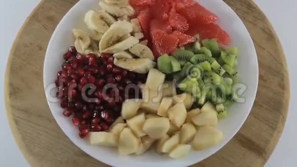 切片的猕猴桃香蕉柚子梨和石榴在白色盘子上旋转水果沙拉原料视频的预览图