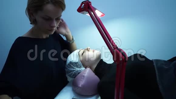 睫毛延伸化妆大师把睫毛伸向一个年轻女孩那个女孩躺着旁边有一盏灯视频的预览图