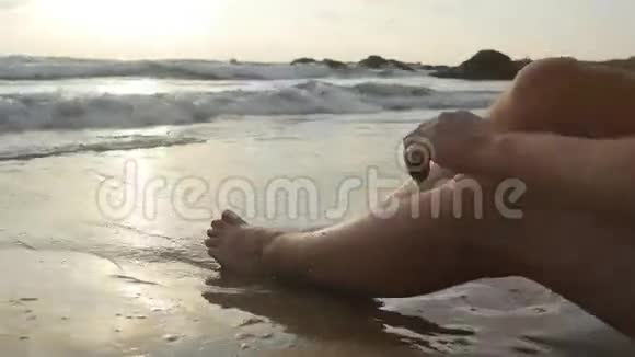 一双女孩的脚躺在海滩上海水冲刷着晒黑的女性腿和身体美丽的年轻女子视频的预览图