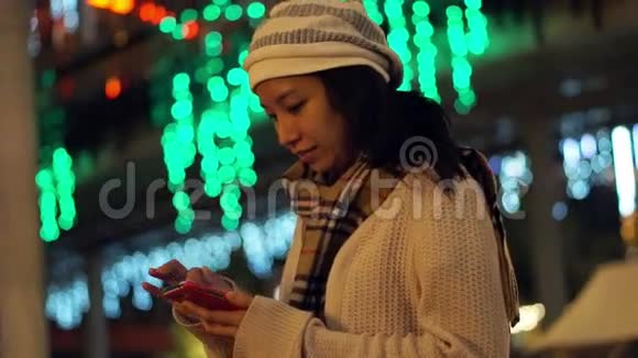 以圣诞灯为背景的亚洲女孩在节日期间使用智能手机的视频通信摘要视频的预览图