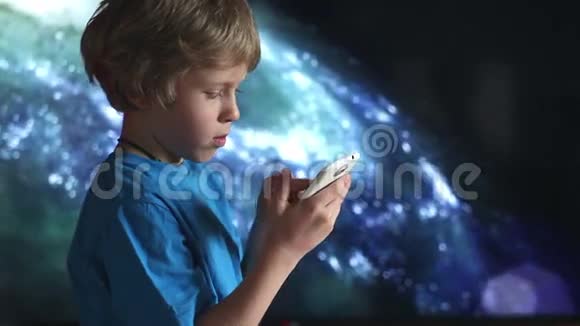 玩智能手机的男孩坐在宇宙天空背景上的男孩和移动设备视频的预览图