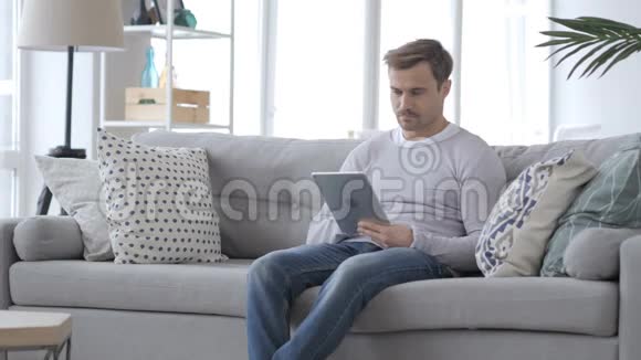 坐在沙发上用平板电脑的成年男子视频的预览图