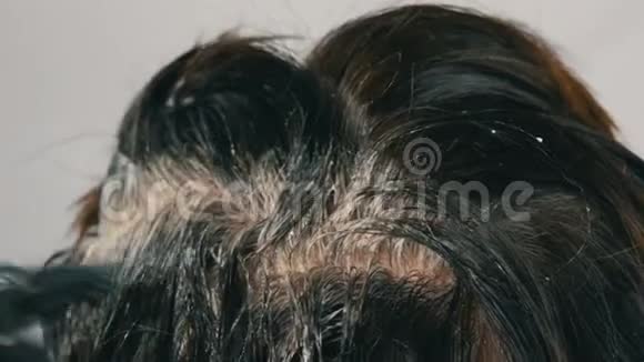 一个中年妇女用特殊的刷子给自己梳头她的灰色根长得过高看上去很近深色头发视频的预览图