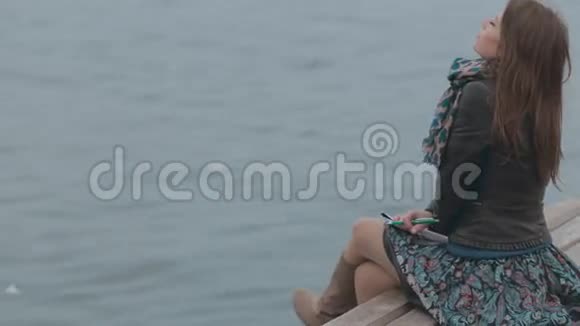 迷人的女孩坐在靠近大海的泊位上视频的预览图