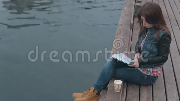 可爱的女孩坐在靠近大海的木墩上视频的预览图