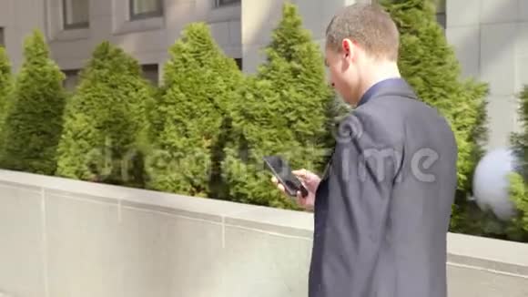 年轻的商人走在街上在智能手机上写一条信息视频的预览图