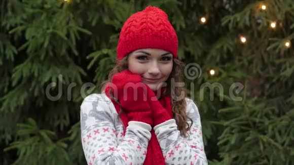 戴着红帽围巾和手套的年轻美女在圣诞树和腰带的背景上晒太阳视频的预览图