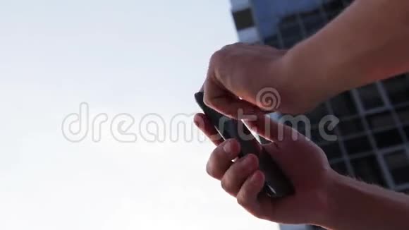 这家伙看着手机背景下美丽的风景玻璃摩天大楼特写视频的预览图