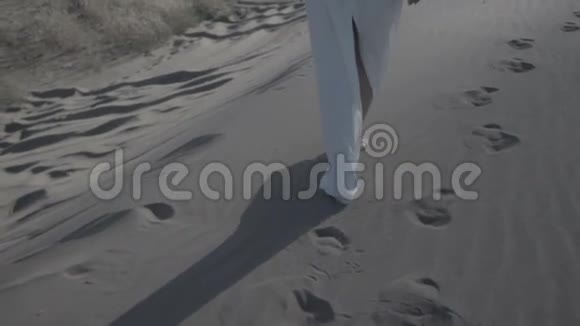 穿着白色连衣裙在沙滩沙丘上行走的女人的脚太阳落山时的阴影是平坦的视频的预览图